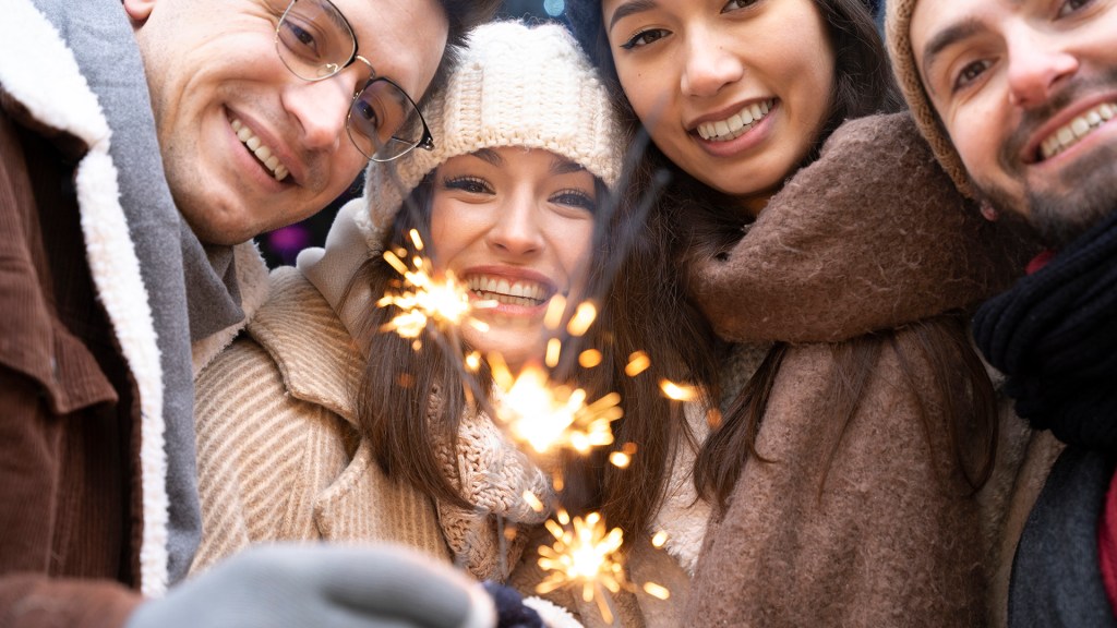 Group of friends smiling together while holding sparklers, symbolizing connection, joy, and shared happiness as a new year begins.